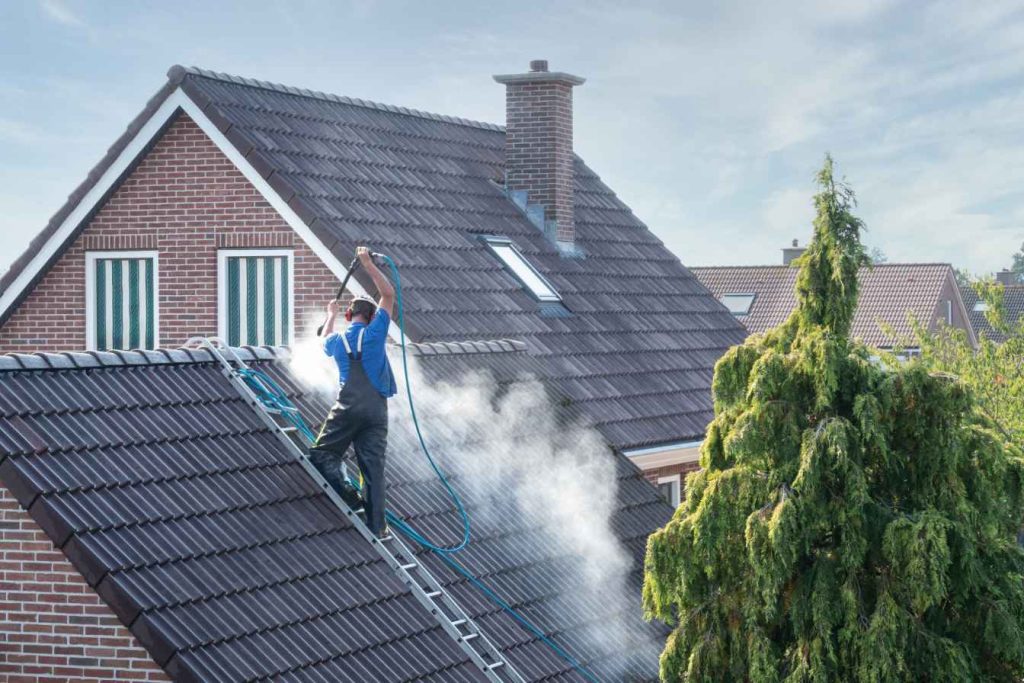 The pressure cleaning contractor is cleaning the black roof shingles of a house in Wollongong NSW.