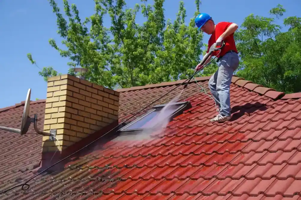 A pressure cleaner is cleaning a red roof tile of a house in Wollongong NSW.